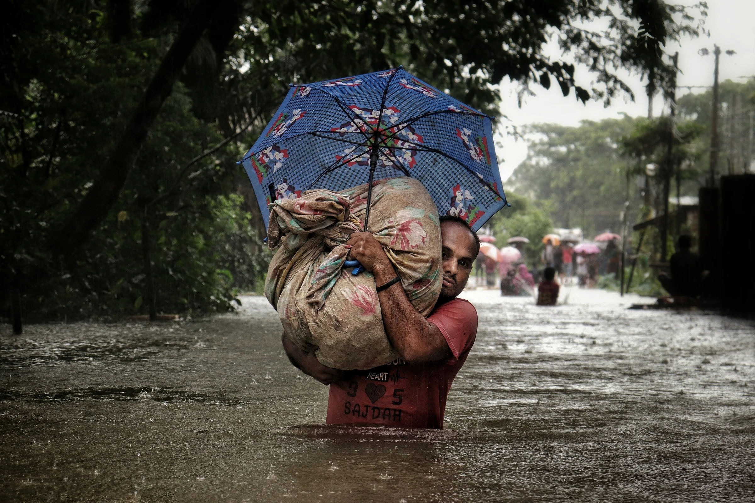 A man carries his belongings through floodwater in Sylhet, 2022
