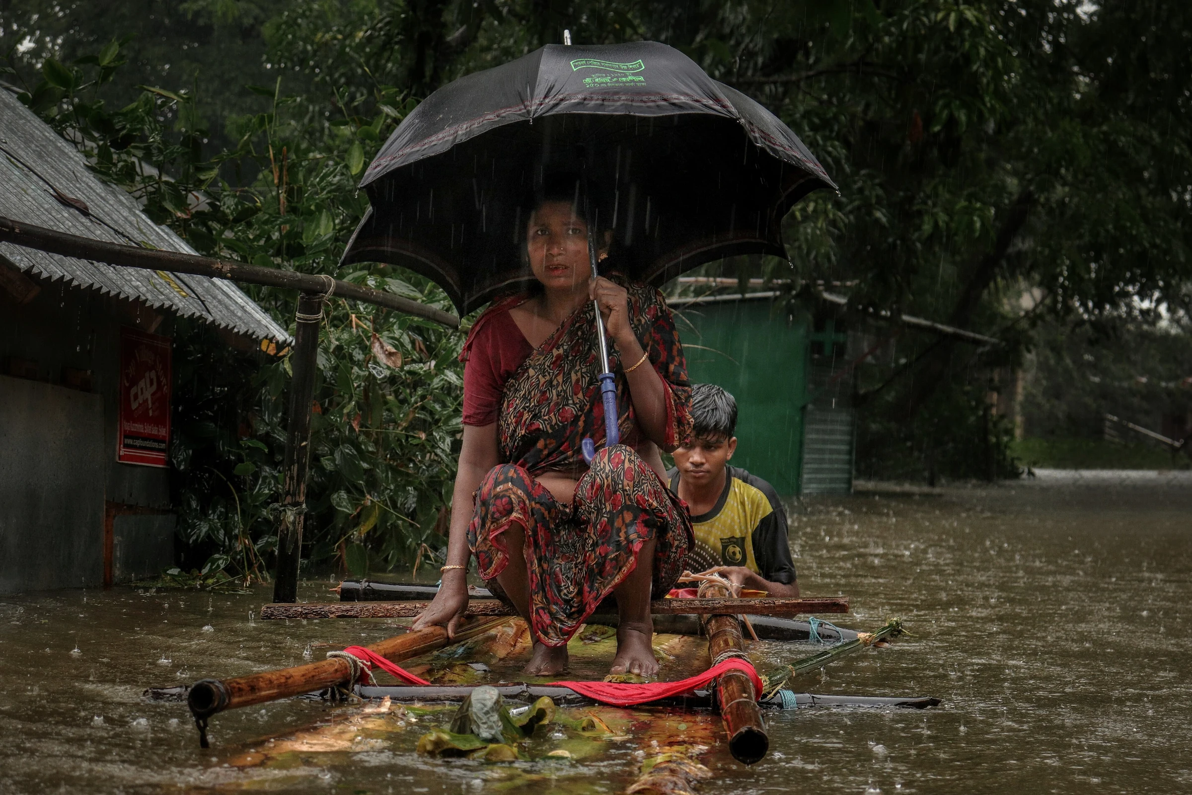 A woman and a boy move to shelter on a bamboo raft during flash floods in Sylhet, 2022
